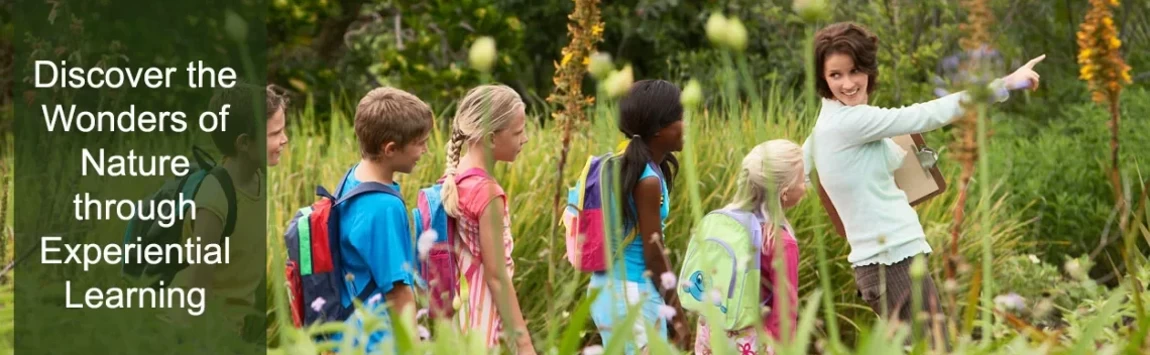 A female teacher leading 5 students walking through a field.